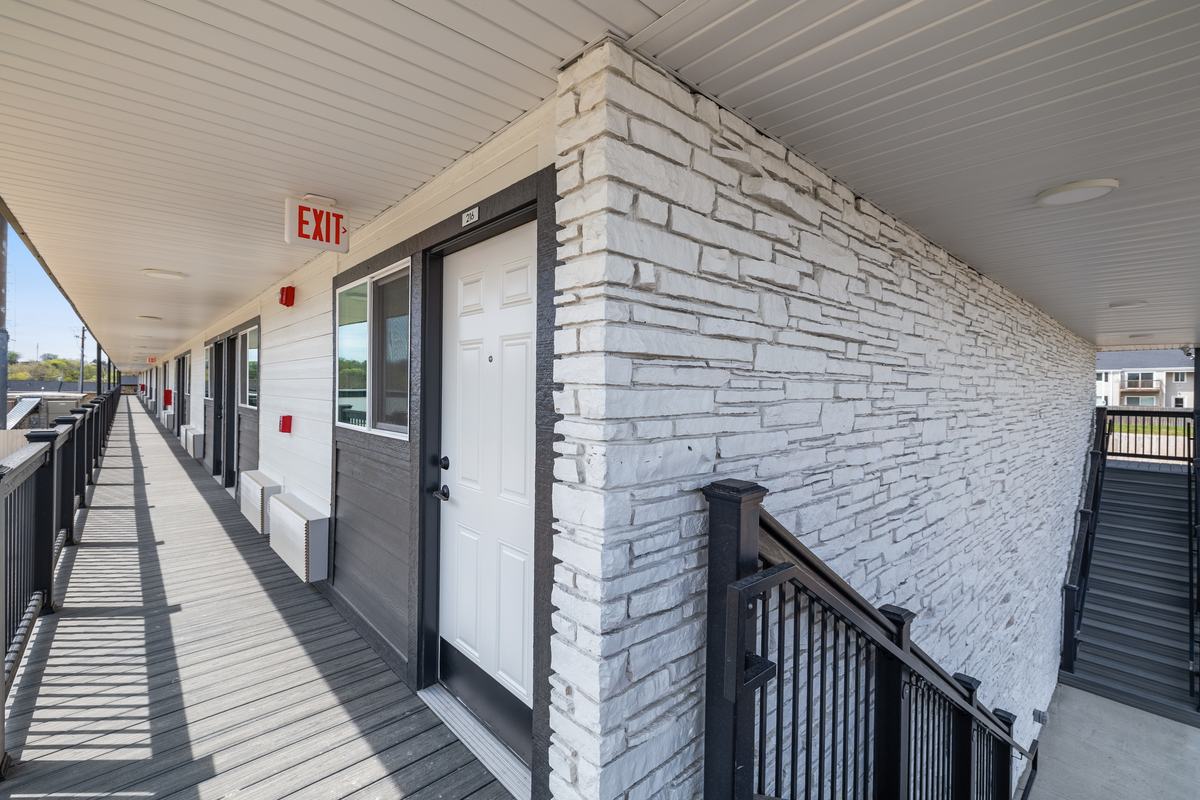 The open second-floor walkway, with whitewashed stone, a private apartment entry door and black steel railing.