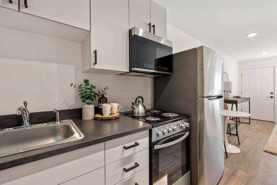 The studio kitchen with stainless steel refrigerator, range, microwave and a dark countertop.