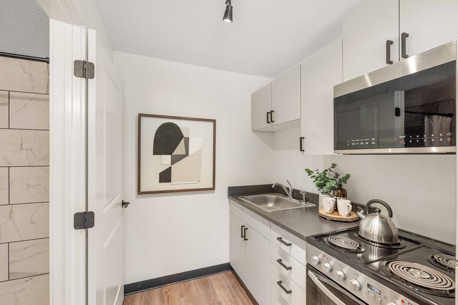 Kitchen cabinetry, stainless range and microwave, seen from the entry of a studio apartment.