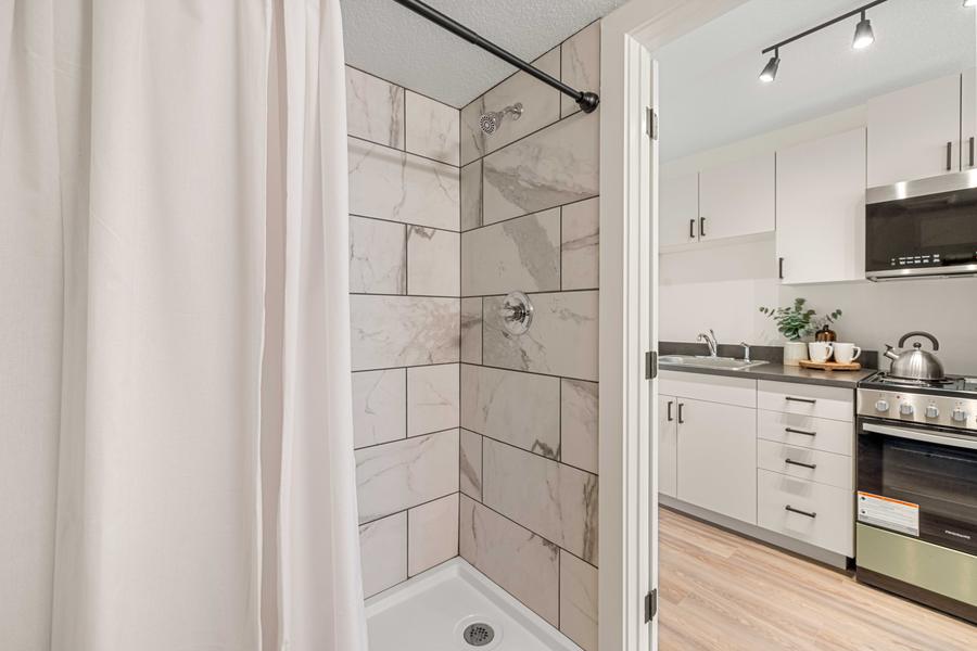 A tiled shower with a glass panel, next to the kitchen in a studio apartment.