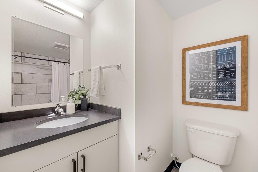 Bathroom vanity with a framed mirror, dark counter and tiled surround.