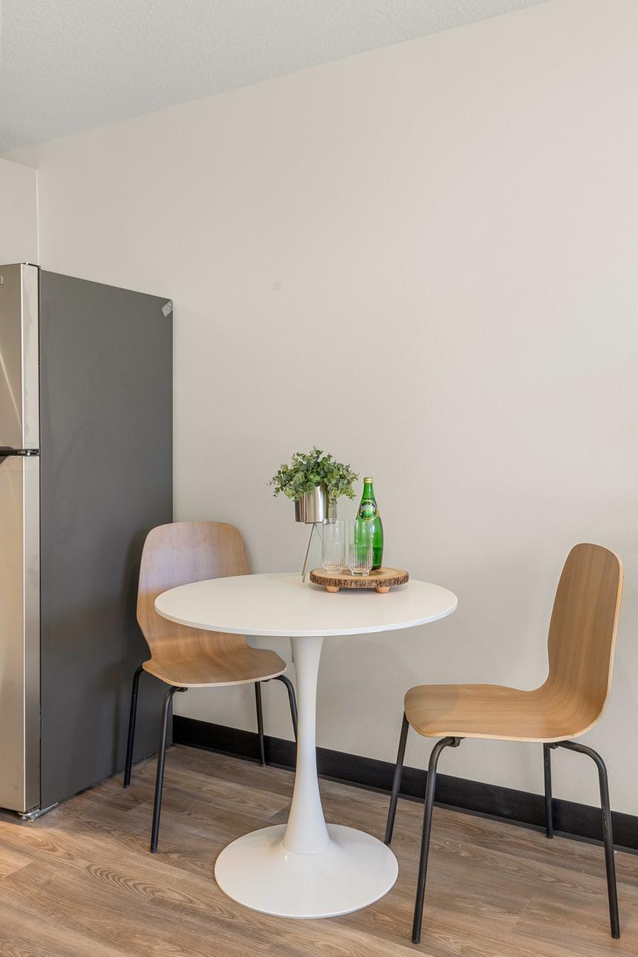A round dining table with two chairs beside the refrigerator in a studio apartment.