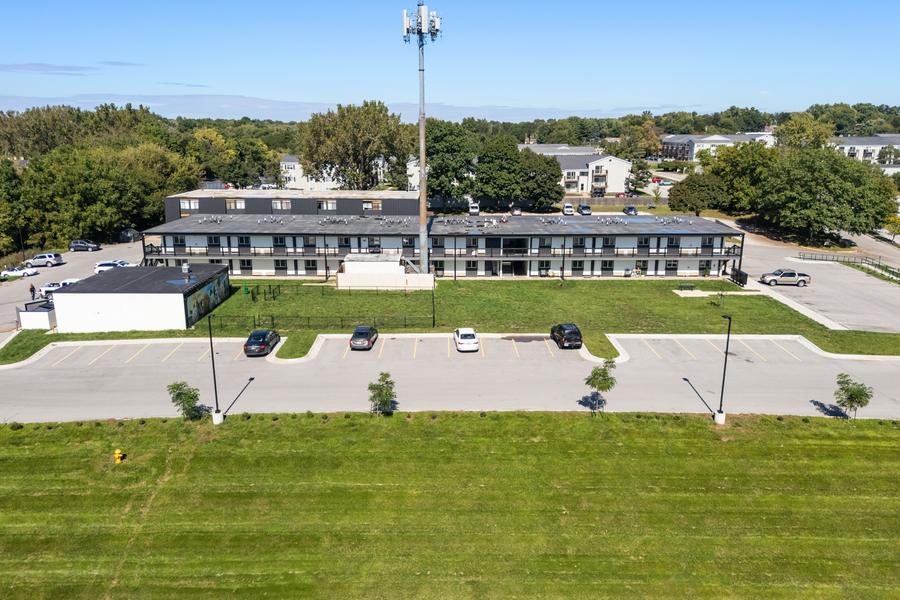 The long side of the building along the parking lot, with young trees and mown grass in front.