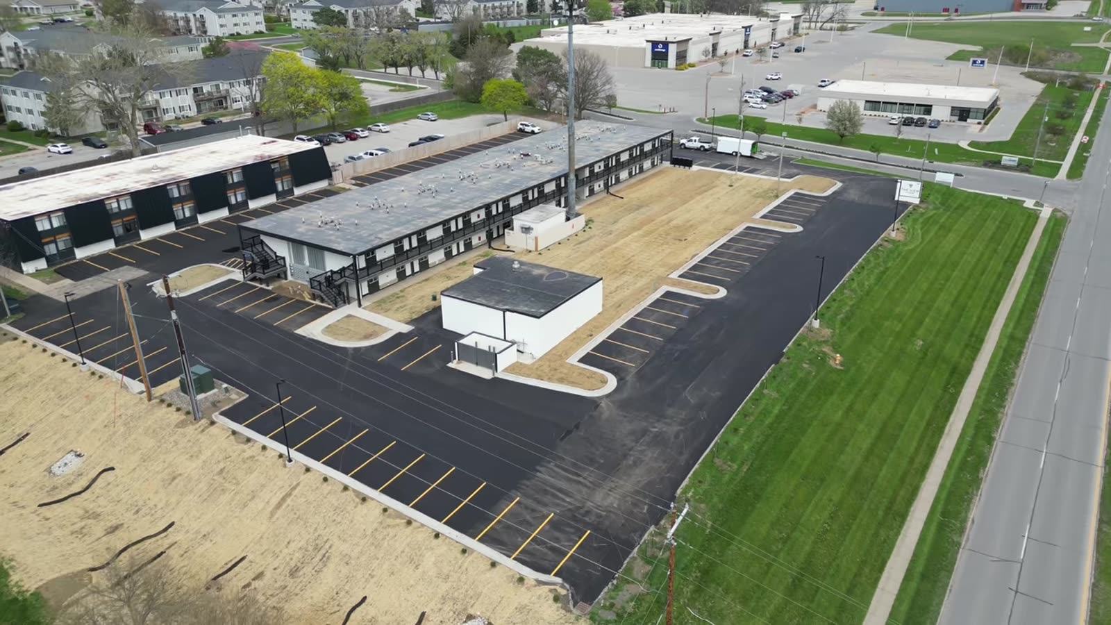 Aerial view of The View on Hickman, a long two-story apartment building with black steel railings and a striped parking lot, in Urbandale, Iowa.