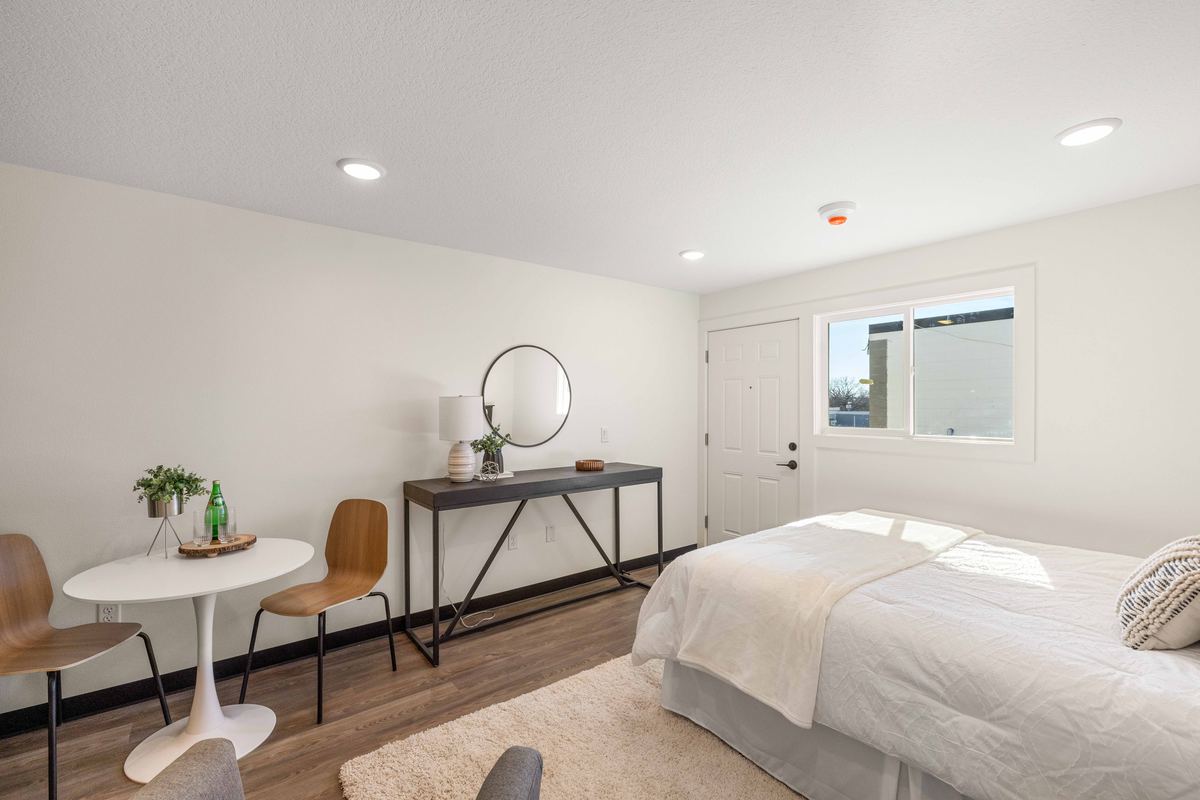 A staged studio apartment with a bed, a dining table for two, framed art and wood-look plank flooring.